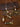 A beaded necklace and matching bracelet displayed on a brown textured surface with decorative paper. The jewelry features multicolored beads in white, red, green, yellow, and brown, along with metallic gold-toned spacer beads and a small engraved gold tag.