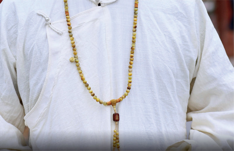 Close-up of a person wearing a white garment with a beaded necklace.