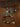 A beaded necklace and matching bracelet displayed on a textured brown surface with engraved cards behind them. The jewelry features turquoise, dark red, black, gray, and metallic gold and silver beads with engraved round charms.