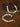 A beaded necklace and matching bracelet displayed on a textured brown surface with decorative script cards. The jewelry features white and pale gray marbled beads, gold-toned spacer beads, and a carved light wood bead, with engraved gold tags attached.