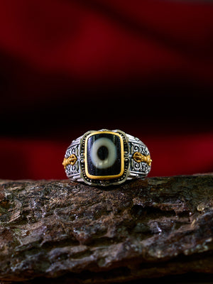 Ring with an eye design on a wooden surface against a red background