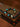 A beaded bracelet with turquoise, black, red, and metallic gold beads, featuring a silver-toned charm engraved with Tibetan script, displayed on a decorative antique-style box with a brown paper overlay.