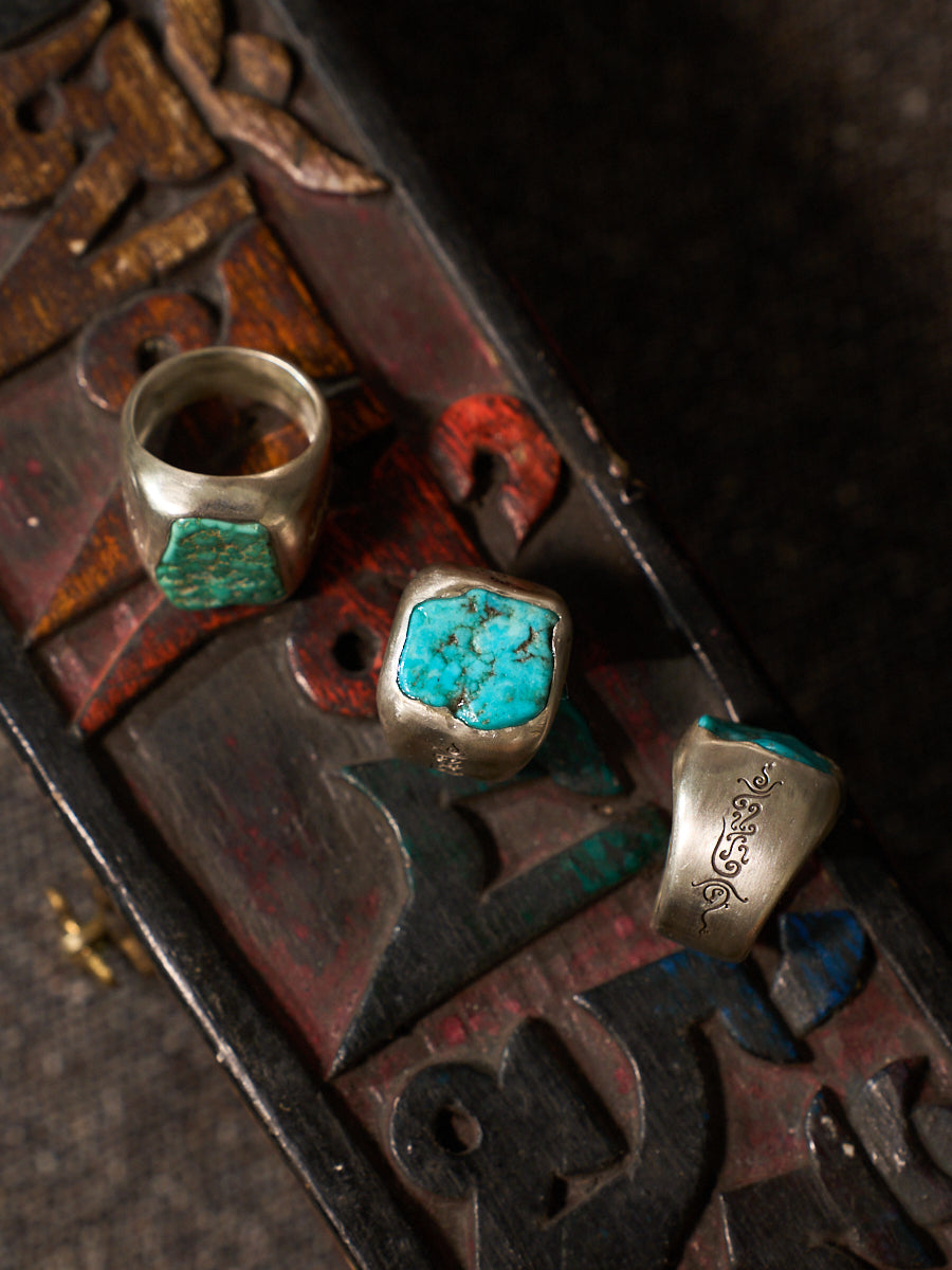 Three silver rings with turquoise stone inlays displayed on a dark carved wooden surface.