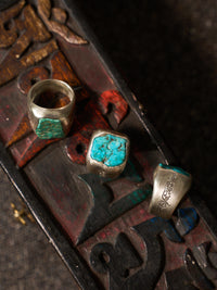 Three silver rings with turquoise stone inlays displayed on a dark carved wooden surface.