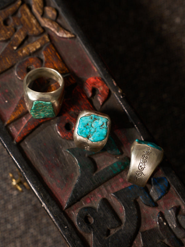 Three silver rings with turquoise stone inlays displayed on a dark carved wooden surface.