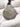 A teardrop-shaped metallic pendant with a textured silver-gray finish and an intricate gold mandala design, resting on a white knit fabric background.