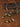 A beaded necklace and matching bracelet displayed on a textured brown surface with decorative stone slabs. The jewelry features polished multicolored beads in brown, gold, red, cream, and black, along with small silver-toned disc charms engraved with 'SANTO'.