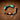 A handmade beaded bracelet with turquoise, green, orange, and brown beads, a silver chain, and a teardrop-shaped silver charm, displayed on a textured brown leather background.
