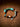 A handmade beaded bracelet with turquoise, green, orange, and brown beads, a silver chain, and a teardrop-shaped silver charm, displayed on a textured brown leather background.